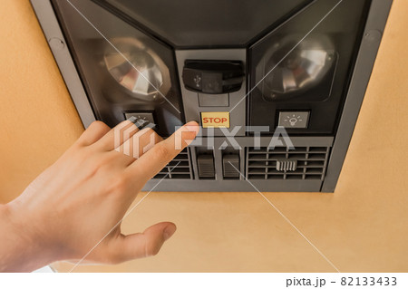 The guy's hand points his finger at the stop button of the air conditioning system in the ceiling of the tourist bus 82133433