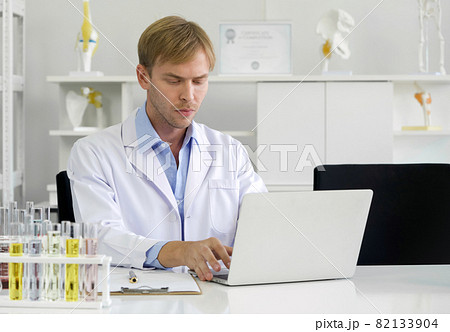 Young caucasian scientist use computers to research chemical compounds on the internet. Working atmosphere in chemical laboratory. Test tubes filled with chemicals on the table. Young caucasian scientist use computers to research chemical compounds on the internet. Working atmosphere in chemical laboratory. Test tubes filled with chemicals on the table. 82133904