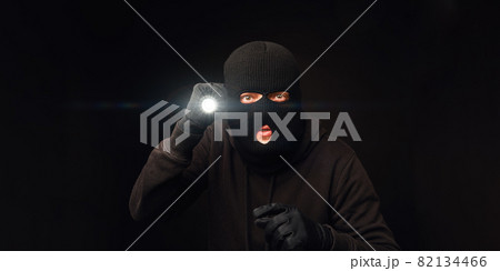 Masked burglar with flashlight on dark back 82134466