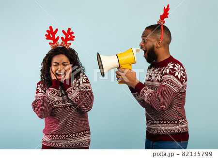 Black man shouting with megaphone loudspeaker at woman, standing together over blue background Black man shouting with megaphone loudspeaker at woman, standing together over blue background 82135799