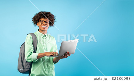 Technology and e-learning concept. Excited black teen guy with laptop and backpack, blue background, empty space 82136093