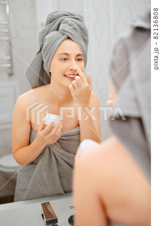 Woman smears her face with white cream for wrinkles and acne in the bathroom. 82136808