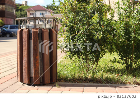 Brown wooden trash can and bush on the street with blurred sunny background. 82137602