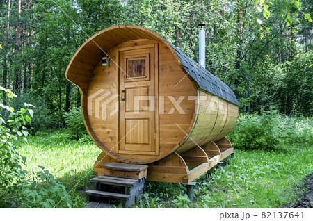 Round wooden barrel bath stands in the forest on a sunny summer day Round wooden barrel bath stands in the forest on a sunny summer day 82137641