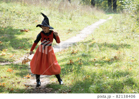 Beautiful girl dressed in a witch costume for Halloween. The witch is dancing. The child is dancing with autumn oak leaves Beautiful girl dressed in a witch costume for Halloween. The witch is dancing. The child is dancing with autumn oak leaves 82138406