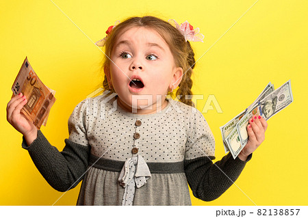 Girl with banknotes in hands on a yellow background, business child with world currency. 82138857