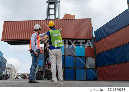 Industrial worker works with co-worker at overseas shipping container yard Industrial worker works with co-worker at overseas shipping container yard 82139023