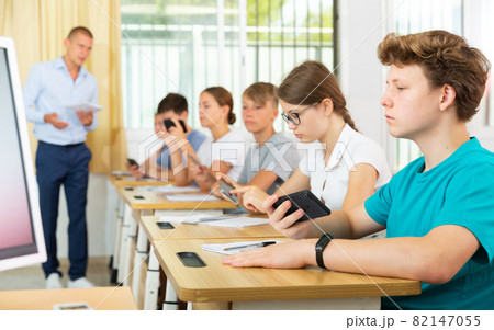 Group of modern teenagers sitting with mobile phones on lesson Group of modern teenagers sitting with mobile phones on lesson 82147055