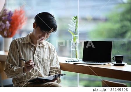 Smiling young man sitting bright office and making note on notebook. 82149508