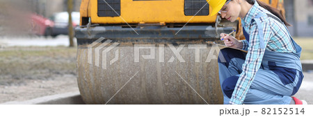Woman examines asphalt pavement in front of asphalt paver 82152514