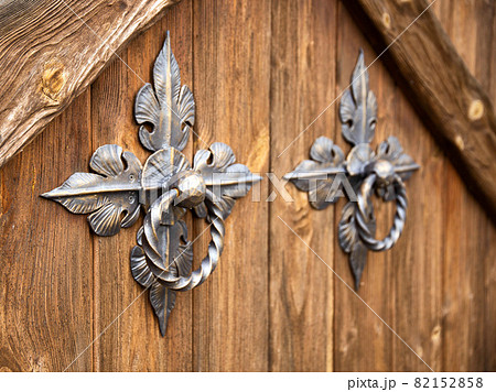 Door handles on a wooden door in the form of forged bronze rings, close-up. Ancient 82152858