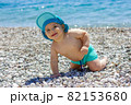Sweet chubby baby on a pebble beach. Blue sea and summer sunshine 82153680