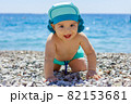 Sweet chubby baby on a pebble beach. Blue sea and summer sunshine 82153681