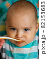 Angry funny baby is spoon fed. Mother feeding her child with pureed vegetables and fruits 82153683