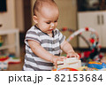 Cute chubby baby stands and plays with a children's music table. Lots of colorful toys everywhere. 82153684