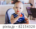 Sweet baby boy eating red watermelon sitting at baby chair in restaurant. Hotel vacation with child 82154320