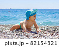 Sweet chubby baby on a pebble beach. Blue sea and summer sunshine 82154321