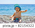 Sweet chubby baby on a pebble beach. Blue sea and summer sunshine 82154322