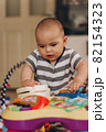 Cute chubby baby stands and plays with a children's music table. Lots of colorful toys everywhere. 82154323