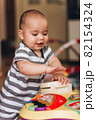 Cute chubby baby stands and plays with a children's music table. Lots of colorful toys everywhere. 82154324