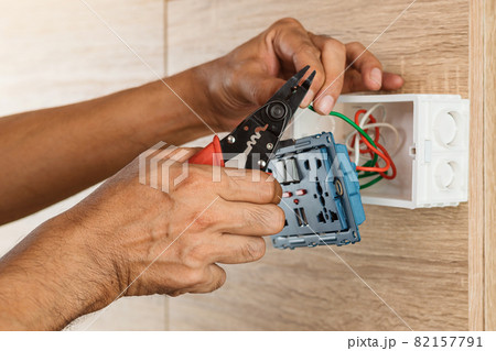 Electrician is stripping electrical wires in a plastic box on a wooden wall to install the electrical outlet. Electrician is stripping electrical wires in a plastic box on a wooden wall to install the electrical outlet. 82157791