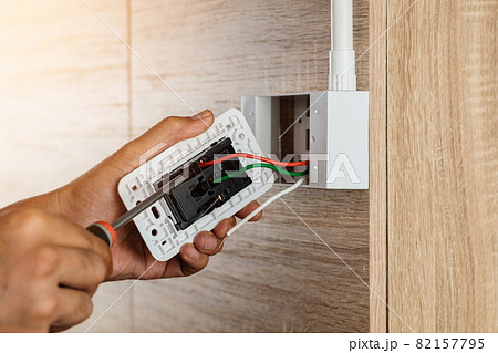 Hand of an electrician is using a screwdriver to attach the wires to the socket. Hand of an electrician is using a screwdriver to attach the wires to the socket. 82157795
