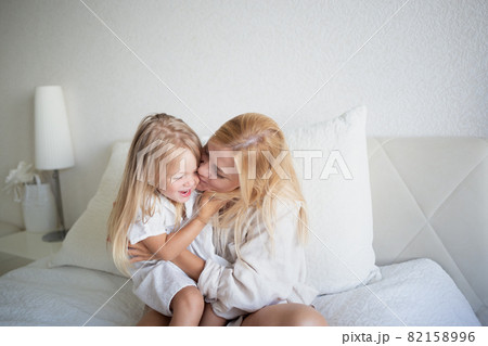 little girl hugging with mom while sitting on the bed in the bedroom 82158996