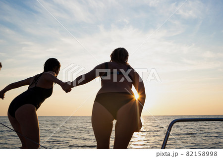 a group of friends jumping into the sea from a yacht at sunset 82158998