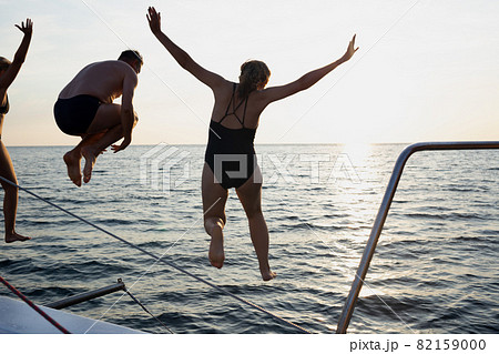 a group of friends jumping into the sea from a yacht at sunset 82159000