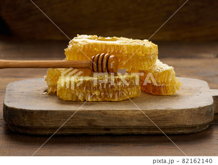 wax honeycomb with honey on a black board and a wooden spoon, brown table 82162140