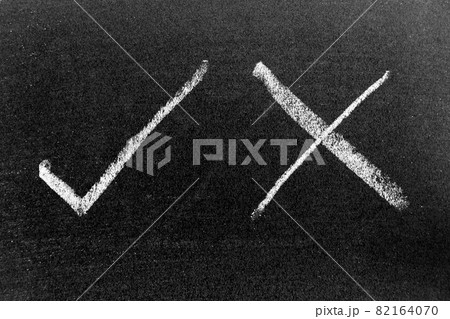 White color chalk hand drawing in check mark of right and wrong shape on black board background White color chalk hand drawing in check mark of right and wrong shape on black board background 82164070