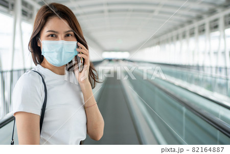 Portrait of a young woman in a medical mask for anti-coronavirus COVID-19 pandemic infectious disease outbreak protection and use a smartphone in Public area. Concept of Virus pandemic and pollution Portrait of a young woman in a medical mask for anti-coronavirus COVID-19 pandemic infectious disease outbreak protection and use a smartphone in Public area. Concept of Virus pandemic and pollution 82164887
