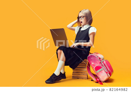 Full length shocked schoolgirl sit on the stack of books work on laptop. Kids education concept. Full length shocked schoolgirl sit on the stack of books work on laptop. Kids education concept. 82164982