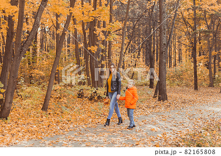 Mother and son walking in the fall park and enjoying the beautiful autumn nature. Season, single parent and children concept. Mother and son walking in the fall park and enjoying the beautiful autumn nature. Season, single parent and children concept. 82165808
