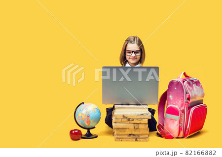 Smiling schoolgirl sit behind a stack of books work on laptop with globe and backpack Kids education Smiling schoolgirl sit behind a stack of books work on laptop with globe and backpack Kids education 82166882