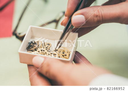 Watchmaker sorting gears in little container with pincers 82166952