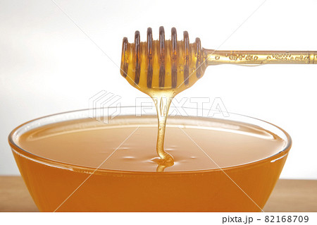 fresh honey dripping from a spoon into a transparent plate on a white background 82168709