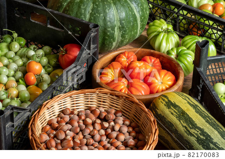 harvest of fresh tomatoes in crates, pumpkin, courgettes and basket with hazelnuts stacked on the floor 82170083