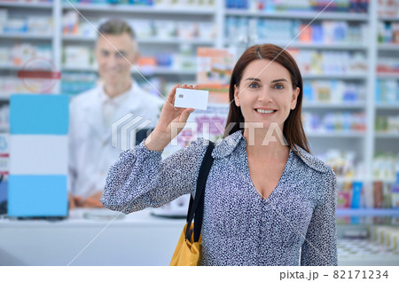 Smiling woman showing credit card at pharmacy Smiling woman showing credit card at pharmacy 82171234