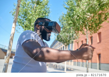 A dark-skinned man in a white tshirt in vr glasses looking excited 82171670