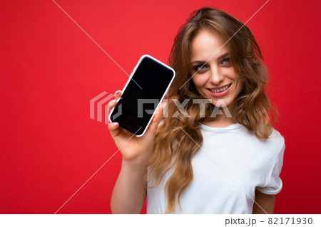 Photo of beautiful smiling young blonde woman good looking wearing white t-shirt standing isolated 82171930
