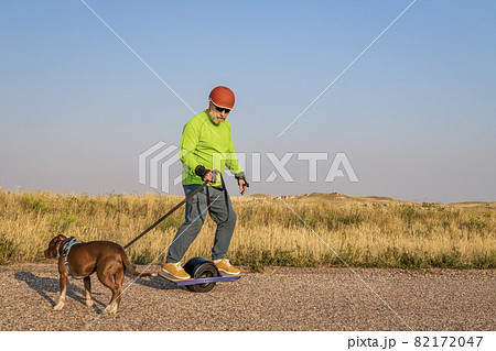 mature senior male is riding one-wheeled electric skateboard  with a dog 82172047