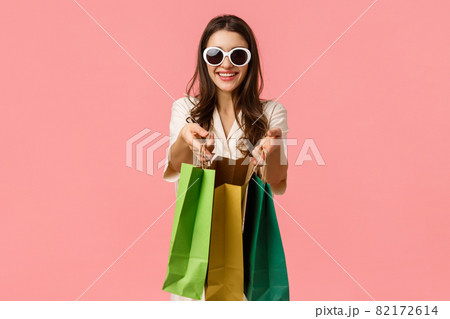 Shopping, consumer concept. Cheerful attractive brunette girl, holding shopping bags and smiling, wearing glasses, enjoying browsing through shop stalls, standing pink background joyful Shopping, consumer concept. Cheerful attractive brunette girl, holding shopping bags and smiling, wearing glasses, enjoying browsing through shop stalls, standing pink background joyful 82172614