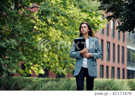 Successful beautiful business woman in suit with document walking to the meeting near modern office building. Successful beautiful business woman in suit with document walking to the meeting near modern office building. 82172876