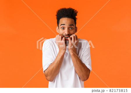 Fear, horror movies, emotions concept. Frightened and insecure, young timid hipster african american male, biting fingernails, staring camera anxious, scared someone know, orange background Fear, horror movies, emotions concept. Frightened and insecure, young timid hipster african american male, biting fingernails, staring camera anxious, scared someone know, orange background 82173815
