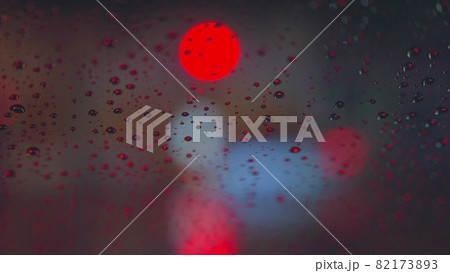 Raindrops run down the glass of the car against the backdrop of the bright lights of the night city. Rainy night. Cars pass the intersection. Bright colored traffic lights. 82173893