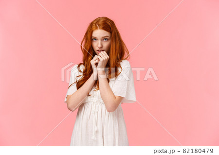Timid kawaii, redhead european girl in white dress, looking shy and cute, blushing, looking from under forehead indecisive and shy, standing modest over pink background 82180479