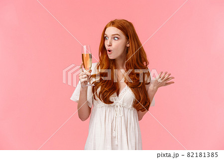 Wow this alcohol hits different. Amused and enthusiastic surprised redhead woman look amazed and wondered and glass with champagne, raising one hand and shrugging, stare curious 82181385