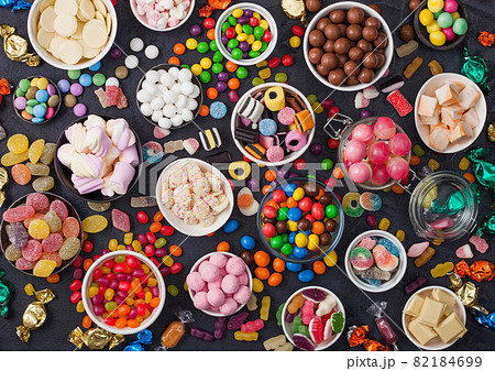 Pink lollipop candies in jar with various milk chocolate and jelly gums candies on black background Pink lollipop candies in jar with various milk chocolate and jelly gums candies on black background 82184699