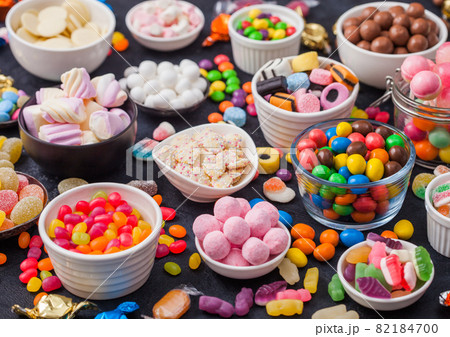Pink lollipop candies in jar with various milk chocolate and jelly gums candies on black background Pink lollipop candies in jar with various milk chocolate and jelly gums candies on black background 82184700